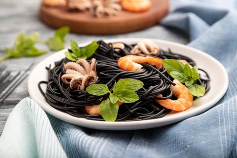 Black cuttlefish ink pasta with shrimps or prawns and small octopuses on gray wooden background and