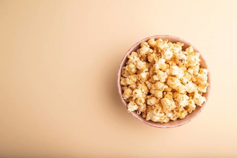 Popcorn with caramel in ceramic bowl on pastel orange background. Top view, flat lay, copy space