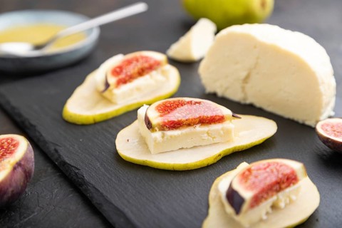 Summer appetizer with pear, cottage cheese, figs and honey on slate board on a black concrete