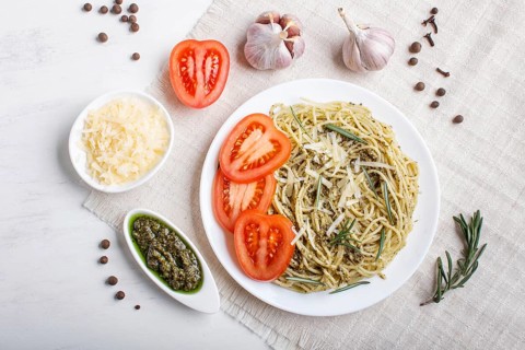 Spaghetti pasta with pesto sauce, tomatoes and cheese on a linen tablecloth on white wooden