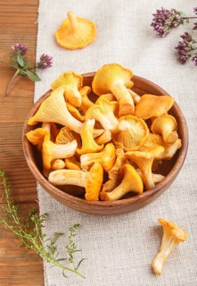 Chanterelle mushrooms in wooden bowl and spice herbs on wooden background with linen textile. side
