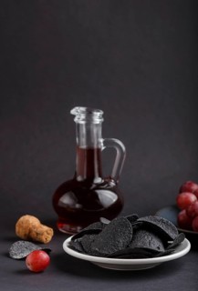 Black potato chips with charcoal, balsamic vinegar in glass, red grapes on a blue ceramic plate on