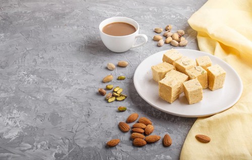 Traditional indian candy soan papdi in white plate with almond, pistache and a cup of coffee on a