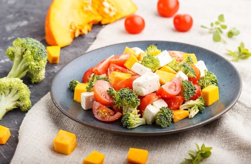 Vegetarian salad with broccoli, tomatoes, feta cheese, and pumpkin on a blue ceramic plate on a