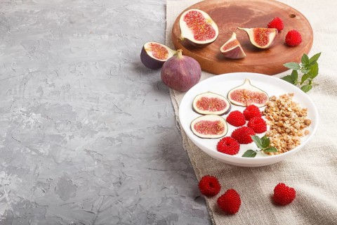 Yoghurt with raspberry, granola and figs in white plate on a gray concrete background and linen