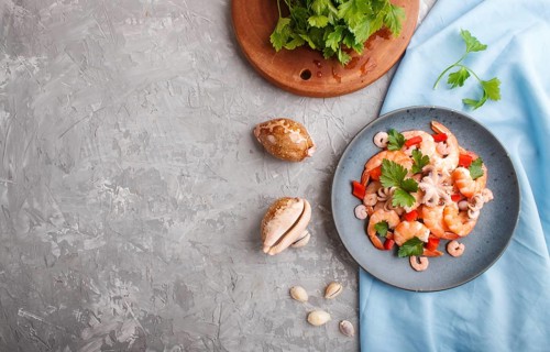 Boiled shrimps or prawns and small octopuses with herbs on a blue ceramic plate on a gray concrete