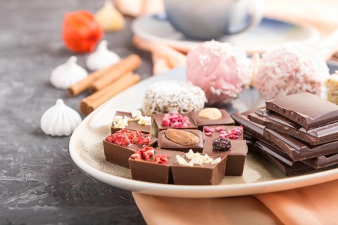 A pieces of homemade chocolate with coconut candies and a cup of coffee on a black concrete