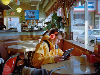 A young individual engrossed in a tablet at a diner table with the warm sunlight streaming through