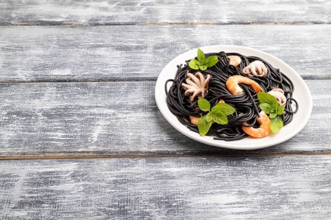 Black cuttlefish ink pasta with shrimps or prawns and small octopuses on gray wooden background.