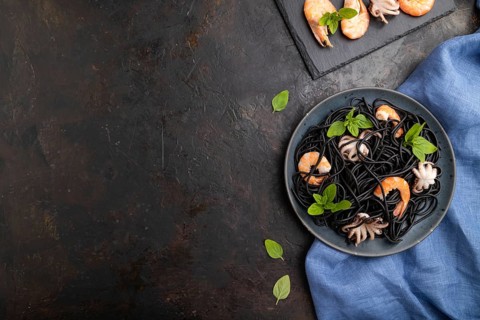 Black cuttlefish ink pasta with shrimps or prawns and small octopuses on black concrete background