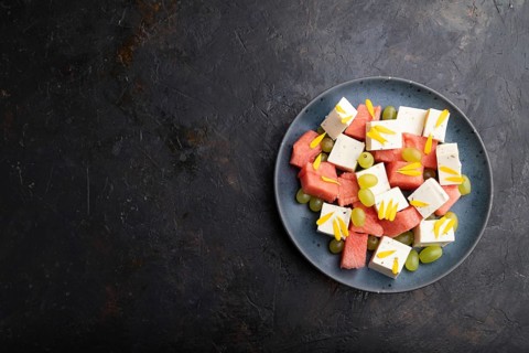 Vegetarian salad with watermelon, feta cheese, and grapes on blue ceramic plate on black concrete