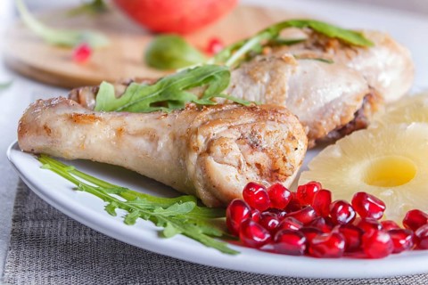 Fried chicken legs with rucola, pineapple and pomegranate seeds on white wooden background, copy