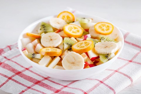 Vegetarian salad of bananas, apples, pears, kumquats and kiwi on linen tablecloth, close up,