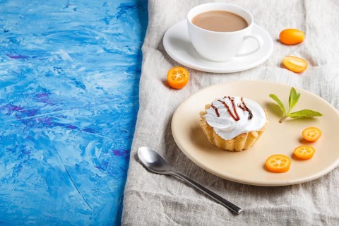 Cake with whipped egg cream on a light brown plate with kumquat slices and mint leaves on a blue