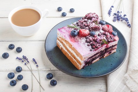Berry cake with milk cream and blueberry jam on blue ceramic plate with cup of coffee and fresh