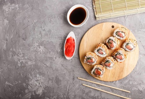 Japanese maki sushi rolls with salmon, sesame, chopsticks, soy sauce and marinated ginger on wooden