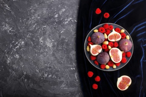 Fresh figs, strawberries and raspberries on blue ceramic plate on black concrete background and