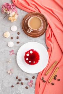 Red cake with souffle cream with cup of coffee on a gray concrete background and red textile. top