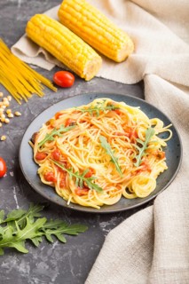 Corn noodles with tomato sauce and arugula on a black concrete background and linen textile. Side