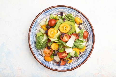 Vegetarian salad of pac choi cabbage, kiwi, tomatoes, kumquat, microgreen sprouts on a white