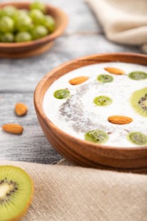 Yogurt with kiwi, gooseberry, chia and almonds in wooden bowl on gray wooden background and linen