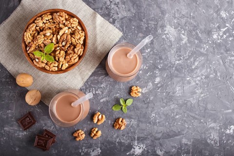 Organic non dairy walnut chocolate milk in glass and wooden plate with walnuts on a black concrete