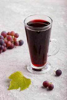 Glass of red grape juice on a gray concrete background. Morninig, spring, healthy drink concept.