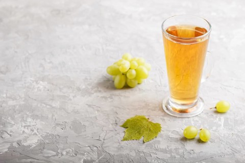Glass of green grape juice on a gray concrete background. Morninig, spring, healthy drink concept.