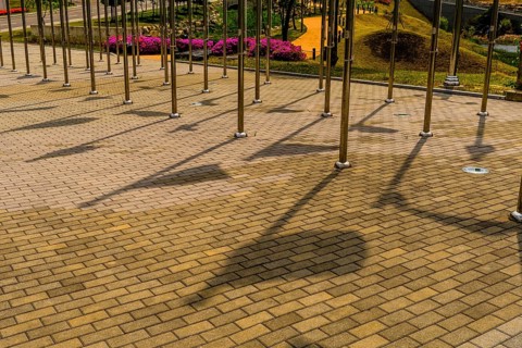 Shadows of flags on brick walkway between rows of chrome flagpoles in public park in South Korea
