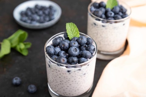 Yogurt with blueberry and chia in glass on black concrete background and orange linen textile. Side