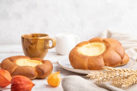 Sour cream bun with cup of coffee on a white wooden and concrete background and linen textile. Side