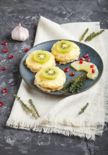 Pieces of baked pork with pineapple, cheese and kiwi on black background, side view, close up