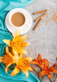 Orange day-lily and lavender flowers and a cup of coffee on a gray concrete background, with blue