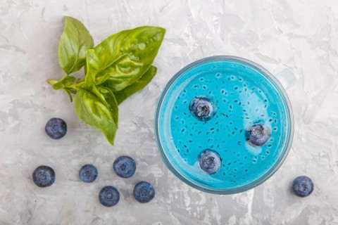 Glass of blueberry blue colored drink with basil seeds on a gray concrete background. Morninig,