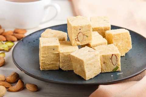 Traditional indian candy soan papdi in a blue ceramic plate with almond, pistache, cashew and a cup