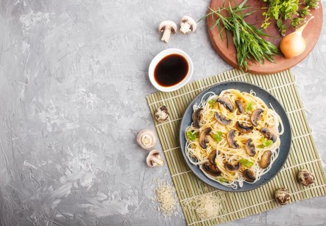 Rice noodles with champignons mushrooms, egg sauce and oregano on blue ceramic plate on a gray