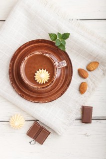 Cup of hot chocolate and pieces of milk chocolate with almonds on a white wooden background with
