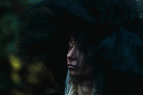 A white thin caucasian blonde woman in shadows wears a large hat, creating a moody and