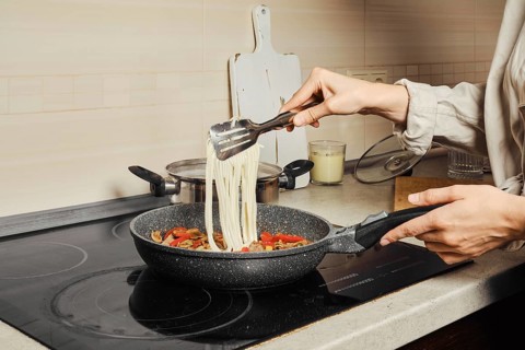 Unrecognizable woman transfers noodles with kitchen tongs into a frying pan with vegetable dressing