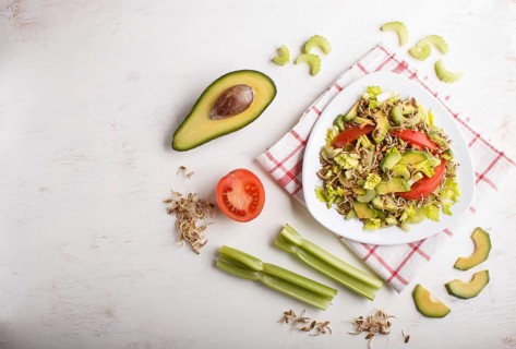 Vegetarian salad of celery, germinated rye, tomatoes and avocado on linen tablecloth, top view,