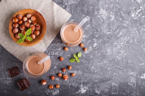Organic non dairy hazelnut chocolate milk in glass and wooden plate with hazelnuts on a gray
