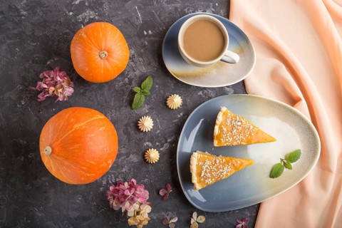 Two pieces of traditional american pumpkin pie with cup of coffee and pumpkins on a black concrete