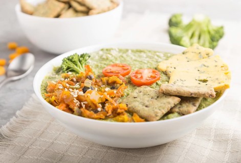 Green broccoli cream soup with crackers and cheese in white bowl on a gray concrete background and