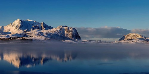 Leichter nebel in der verschneiten Berglandschaft auf den vesteralen mit schoener Spiegelung im