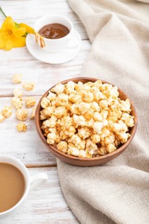 Popcorn with caramel in wooden bowl and a cup of coffee on a white wooden background and linen