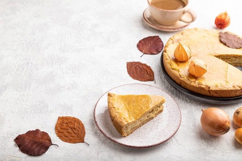 Autumn onion pie decorated with leaves and cup of coffee on gray concrete background. Side view,