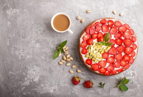 Homemade cake with yoghurt cream, strawberry, pistachio and a cup of coffee on a gray concrete