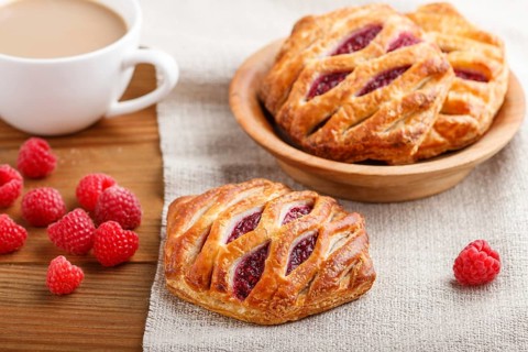 Puff pastry buns with strawberry jam on wooden background with linen textile and a cup of coffee.