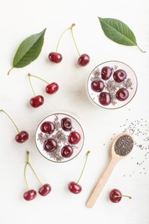 Yoghurt with cherries, chia seeds and granola in glass with wooden spoon on white wooden background
