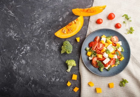 Vegetarian salad with broccoli, tomatoes, feta cheese, and pumpkin on a blue ceramic plate on a